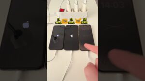Imagen de tres iPhone alineados sobre una mesa conectados a una regleta para una prueba de carga y arranque, con etiquetas que los identifican como 11 Pro, 12 Pro y 13 Pro, el logo de Apple visible en las pantallas de dos de ellos y un dedo tocando el de la derecha, Xiaomi 13 Pro ventajas y desventajas: ¿vale la pena su cámara?