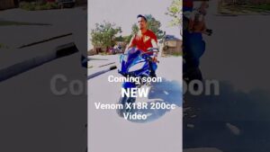 Hombre con camiseta naranja montado en una moto deportiva azul en una calle residencial soleada con casas y árboles al fondo, vista frontal que muestra el carenado, el parabrisas y los espejos, Ventajas y desventajas de la RT200: ¿vale la pena esta moto?