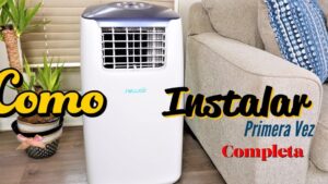 Unidad blanca de aire acondicionado portátil situada junto a un sofá beige y una planta en un salón con persianas, presentada como imagen instructiva para instalación y uso doméstico con enfoque en accesibilidad y palabras clave para buscadores, Ventajas y desventajas aire acondicionado portátil: ¿vale la pena?