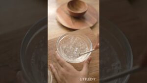 Manos batiendo un gel transparente en un cuenco de cristal sobre una tabla de madera junto a pequeños recipientes de madera, imagen que ilustra Ventajas y desventajas del aloe vera en la cara para tu piel y su preparación casera para el cuidado facial.