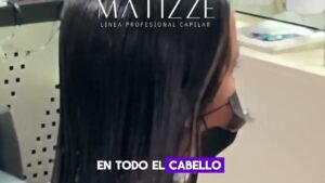 Persona con mascarilla sentada en un salón de belleza con el cabello largo, oscuro y humedecido tras la aplicación de un tratamiento capilar aplicado en todo el cabello, imagen adecuada para ilustrar Aminoácidos para el cabello ventajas y desventajas reales.