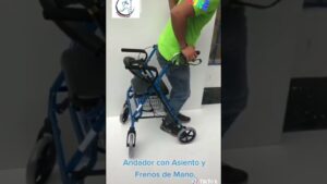 Persona con camiseta verde y jeans apoyándose en un andador para adultos azul con asiento acolchado, cesta inferior y frenos de mano visibles, demostrando su uso y estabilidad sobre ruedas en un fondo claro — Ventajas y desventajas del andador para adultos para movilidad segura