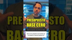 Hombre gesticulando frente a la cámara en formato vertical dentro de una oficina con ventana a edificios y un gran titular amarillo "PRESUPUESTO BASE CERO" sobrepuesto y un recuadro de pregunta en español, ilustrando Ventajas y desventajas presupuesto base cero para optimizar recursos.