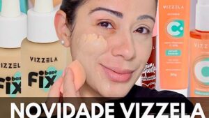 Primer plano de una mujer aplicando base líquida con una esponja en la mejilla mientras sonríe, rodeada de botellas y envases de cosméticos y un rótulo promocional que sugiere una reseña de maquillaje y cuidado facial, Citología en base líquida ventajas y desventajas: impacto en tu salud.