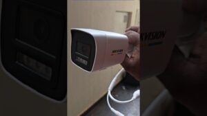 Primer plano de una cámara de seguridad tipo bullet blanca de la marca Hikvision sostenida por una mano con cables y conectores visibles, lente y LEDs integrados, imagen optimizada para accesibilidad y SEO enfocada en vigilancia e instalación, Ventajas y desventajas de un NVR: ¿es la mejor opción para ti?
