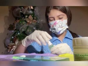 Una persona con mascarilla decorada y guantes de látex manipula un frasco pequeño y polvo blanco sobre una superficie junto a un envase plástico frente a un árbol navideño, Carboxilato de zinc ventajas y desventajas: descubre su impacto real