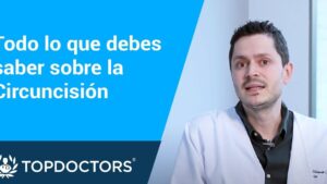 Banner informativo dividido con panel azul que muestra el texto "Todo lo que debes saber sobre la Circuncisión" a la izquierda y a la derecha un médico joven con bata blanca hablando frente a cámara junto al logotipo de TOPDOCTORS, Circuncisión en adultos ventajas y desventajas que debes conocer