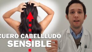 Hombre con bata blanca explicando frente a la cámara junto a la imagen de una mujer de espaldas que se toca el cuero cabelludo con una flecha roja ascendente y el texto grande "CUERO CABELLUDO SENSIBLE", Ventajas y desventajas de usar gorra y su impacto en el cabello.