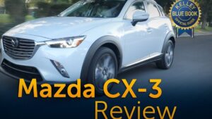 Vista frontal lateral de un Mazda CX-3 blanco en movimiento por una carretera arbolada con las ruedas en giro, texto grande sobreimpuesto que dice "Mazda CX-3 Review" y un sello de la guía Kelley Blue Book en la esquina, Ventajas y desventajas del Mazda CX 3: ¿vale la pena comprarlo?