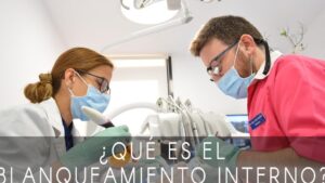 En una clínica dental dos profesionales con mascarillas, gafas y guantes trabajan bajo una lámpara dental junto a instrumental y equipos odontológicos, ilustrando Blanqueamiento dental interno ventajas y desventajas: ¿es para ti?