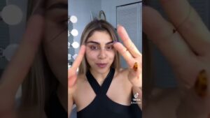 Primer plano de una mujer frente a un espejo iluminado que sostiene un hilo entre los dedos para mostrar la técnica de depilación de cejas en estilo tutorial, Depilación con hilo ventajas y desventajas: ¿es ideal para ti?