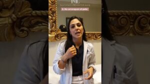 Mujer profesional con bata blanca y cabello oscuro gesticula explicando en un consultorio frente a un espejo dorado ornamentado, con un rótulo que indica "2. No arranques el pelo" y el logotipo visible, Ventajas y desventajas de la depilación láser en axilas: guía esencial