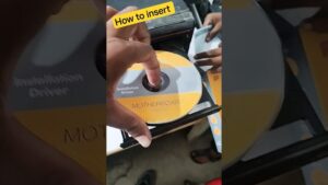 Manos insertando un CD de instalación etiquetado MOTHERBOARD en la bandeja desplegada de una unidad de CD-ROM abierta, otra persona sostiene el embalaje y hay un rótulo amarillo con "How to insert", Ventajas y desventajas del cd rom: usos y limitaciones clave
