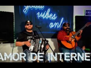 Dúo musical sentado en un pequeño escenario, uno tocando acordeón y el otro guitarra con micrófonos frente a ellos y ambos con gafas de sol y gorras, sobre un fondo de neón que dice "good vibes only" y un texto frontal "AMOR DE INTERNET", descripción accesible y optimizada para SEO que destaca música en vivo, instrumentos acústicos y ambiente íntimo — Ventajas y desventajas del internet en www diferenciador com