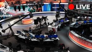 Imagen de una moderna sala de redacción y plató televisivo con mesas curvadas llenas de monitores, cámaras sobre grúas, técnicos trabajando y un presentador frente a una gran pantalla panorámica en una transmisión en vivo, con el mensaje Ventajas y desventajas del trabajo online: descubre si es para ti