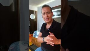 Hombre de mediana edad sentado en una habitación doméstica mirando a cámara y hablando, con micrófono de solapa y manos entrelazadas frente a muebles y una cama al fondo, Eritorbato de sodio ventajas y desventajas y su impacto en alimentos.