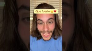 Joven de cabello largo y barba ligera, vestido con camiseta azul y frente a persianas, mira a cámara con expresión intensa y boca entreabierta mientras un rótulo amarillo arriba reza "Que fuerte" con emojis, en una imagen vertical que sugiere contenido informativo sobre 'Ventajas y desventajas del asilo político en Estados Unidos'.