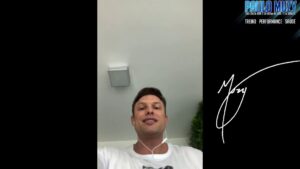 Autorretrato vertical de un hombre joven visto desde un ángulo bajo con auriculares y camiseta blanca frente a un techo con lámpara empotrada y una planta a la derecha, con franjas laterales negras y un área con logotipo y firma, redactado para accesibilidad y optimizado para SEO incluyendo la frase Ventajas y desventajas geográficas de la forma física de Panamá.