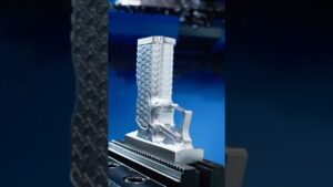 Pieza de aluminio recién fresada con superficie pulida y patrón texturizado en relieve similar a una empuñadura, sujeta en una mordaza de máquina herramienta sobre un fondo azul con marcas de corte visibles, Ventajas y desventajas de la fresadora CNC: ¿vale la pena?