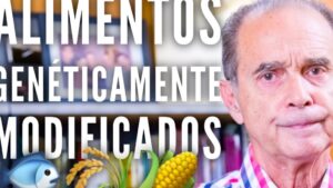Un hombre mayor aparece a la derecha con expresión seria frente a una estantería de libros mientras a la izquierda se leen en grandes letras blancas las palabras "ALIMENTOS GENÉTICAMENTE MODIFICADOS" acompañadas de iconos de pescado, granos y una mazorca de maíz, Ventajas y desventajas del uso de los OGM: descubre su impacto real.