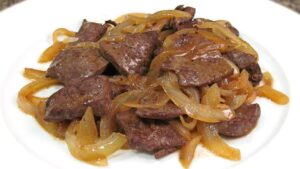 Plato de trozos de hígado de vaca salteado con cebollas doradas y brillo aceitoso sobre un plato blanco, imagen ideal para ilustrar Ventajas y desventajas de comer hígado de vaca saludable.