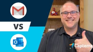 Imagen dividida con fondo azul que muestra a la izquierda los iconos de Gmail y Outlook separados por "VS" y a la derecha un hombre adulto sonriente con gafas y pulgar en alto delante de una estantería con una figura de Spiderman y el logo de Capterra, ilustrando el tema 'Ventajas y desventajas de Hotmail y Gmail: cuál elegir'.