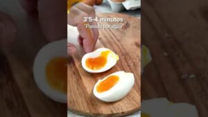 Huevo cocido partido por la mitad con la clara firme y la yema blanda y brillante sobre una tabla de madera mientras una mano sostiene una mitad, imagen clara sobre textura y presentación para recetas y nutrición; Ventajas y desventajas del huevo cocido: descubre si es ideal para ti