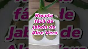 Imagen vertical que muestra un plato con tres jabones redondos verde claro sobre una mesa de madera, hojas de sábila frescas colocadas detrás y un rótulo rosa y blanco sobrepuesto que dice "Receta fácil de Jabón de Aloe Vera", Ventajas y desventajas del jabón de sábila para tu piel.