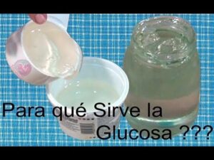Mano que vierte un jarabe transparente y viscoso desde un vaso desechable hacia un envase plástico junto a un frasco de gel sobre una tela a cuadros azul con texto superpuesto Para qué Sirve la Glucosa ???, Jarabe de glucosa ventajas y desventajas: impacto real en salud