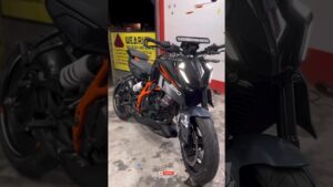 Vista frontal y ligeramente en tres cuartos de una motocicleta naked negra con chasis y detalles naranja, faros LED encendidos y ambiente de taller, Ktm duke 390 ventajas y desventajas: descubre si esta moto es para ti