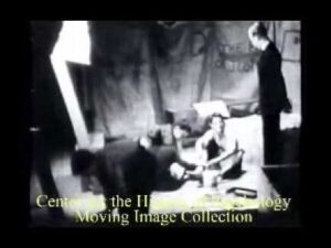 Fotografía histórica en blanco y negro de estilo documental que muestra a cuatro personas en un interior tipo estudio —tres sentadas en el suelo en actitud conversacional y una de pie junto a papeles y objetos esparcidos— con iluminación teatral y composición íntima, ideal para ilustrar contenidos sobre liderazgo y cambio; Ventajas y desventajas del modelo de Kurt Lewin: guía esencial