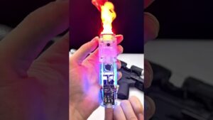 Mano que sostiene un encendedor transparente con circuito y luces LED visibles que emite una llama amarilla-anaranjada sobre un fondo oscuro con objetos desenfocados, Uñas en gel ventajas y desventajas: descubre si son ideales para ti