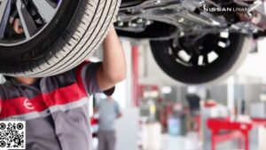 Vista cercana de la llanta y la parte inferior de un coche elevado en un taller con un técnico revisando componentes, ideal para ilustrar búsquedas sobre Llantas con nitrógeno ventajas y desventajas: ¿vale la pena? y temas de seguridad, presión y mantenimiento.