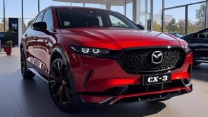 SUV compacto rojo metalizado en vista frontal tres cuartos dentro de un concesionario con parrilla negra brillante y emblema centrado, faros LED angulares, llantas negras de aleación y reflejos en la carrocería, pensado para búsquedas sobre Mazda CX 3 ventajas y desventajas para decidir si vale la pena