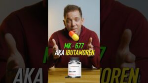 Hombre de mediana edad con sudadera granate sentado detrás de una mesa gesticulando hacia la cámara mientras en la imagen se muestra una cápsula ilustrada y un frasco etiquetado MK-677 junto al texto promocional MK-677 AKA IBUTAMOREN, presentando información de Ventajas y desventajas del mk 677: efectos y riesgos reales.
