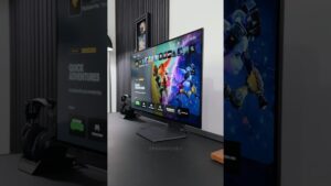 Fotografía de un monitor LCD de biseles delgados mostrando una interfaz de videojuegos colorida sobre un escritorio minimalista con soporte para auriculares, lámpara y paneles acústicos verticales en el fondo, descripción optimizada para accesibilidad y SEO que invita a evaluar rendimiento, diseño y uso diario: Ventajas y desventajas del monitor lcd: ¿es la mejor opción?