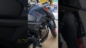 Imagen en primer plano de una motocicleta Italika gris exhibida en sala de exposición que resalta el motor, el radiador con etiqueta, el guardabarros y la llanta delantera con aro rojo, ideal para acompañar contenido informativo y optimizado sobre Ventajas y desventajas de motos Italika: ¿valen la pena?