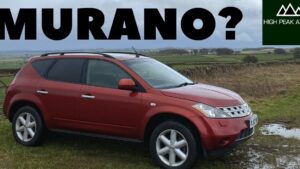 Nissan Murano 2005 ventajas y desventajas para decidir tu compra: SUV rojo visto de perfil estacionado sobre césped y barro junto a charcos, con rieles de techo, llantas de aleación de cinco radios, parrilla cromada y un paisaje rural con cielo nublado de fondo.