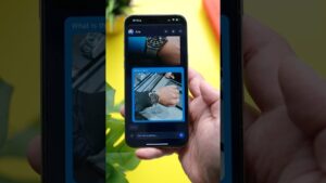 Mano sosteniendo un smartphone en primer plano que muestra una interfaz de asistente visual con fotos de un reloj de pulsera sobre un fondo amarillo y hojas verdes, imagen de alta claridad y contraste pensada para accesibilidad y optimización SEO, Ventajas y desventajas del navegador Opera: ¿es la mejor opción?