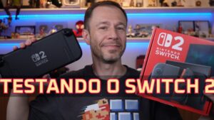 Hombre adulto sonriente en un estudio de reseñas sostiene una consola portátil negra y la caja roja de la nueva Nintendo Switch frente a estanterías con figuras y luces LED azules en una miniatura de vídeo de unboxing y prueba, Ventajas y desventajas Nintendo Switch Lite: ¿vale la pena?