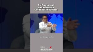 Hombre con camisa blanca y gafas gesticulando en un estudio con mapa mundial de fondo, textos superpuestos y logo de Pro Inversión, ilustrando Ventajas y desventajas de obras por impuestos: impacto real.