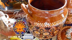Varias ollas de barro tradicionales esmaltadas y decoradas a mano con motivos florales en tonos terracota y anaranjados, una tapa y una pequeña figura de cerámica junto a un emblema colorido de sol y el texto "Cocina Mexicana", perfectas para ilustrar Ventajas y desventajas de ollas de barro: ¿son ideales para ti?