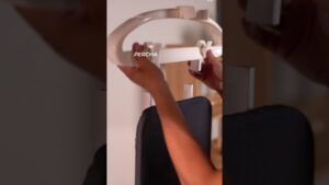 Manos colocan una percha blanca en la parte superior de un tablero de planchar acolchado negro apoyado en una estructura de madera, mostrando un accesorio de montaje y organización para planchado; Plancha de vapor pelo ventajas y desventajas: ¿vale la pena usarla?
