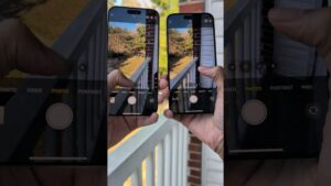 Manos sosteniendo dos teléfonos uno junto al otro que muestran la interfaz de la cámara en modo FOTO mientras capturan desde un balcón la barandilla blanca y árboles con hojas otoñales reflejados en las pantallas para una comparativa de color, brillo y encuadre — Ventajas y desventajas iPhone 16 Pro Max: ¿vale la pena?