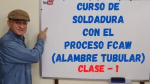 Un hombre con gorra señala un pizarrón blanco donde en letras grandes azules y rojas se lee el anuncio de un curso de soldadura con el proceso FCAW (alambre tubular) junto al logotipo de YouTube, imagen clara y accesible que incorpora la idea clave Ventajas y desventajas del proceso FCAW en soldadura eficaz para mejorar la comprensión de usuarios y lectores de pantalla.