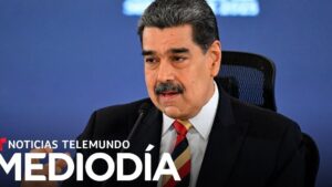 Hombre de mediana edad con bigote y traje oscuro hablando frente a un micrófono y un fondo azul con el logotipo de Noticias Telemundo Mediodía, gesto serio y postura formal, imagen informativa pensada para un reportaje sobre Ventajas y desventajas de la posición geográfica de RD y su impacto