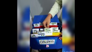 Organizador azul de cartulina con separadores alfabéticos y tarjetas manuscritas (se aprecian letras S, M y A), una mano extrae una tarjeta que dice Aguas claras y en el frente hay un rótulo con la palabra CALDAS, Ventajas y desventajas del sistema alfabético: claves esenciales
