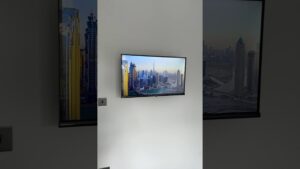 Televisor de pantalla plana montado en una pared blanca que muestra en alta definición un paisaje urbano con rascacielos y canales, con ventanas oscuras a ambos lados que reflejan la misma imagen, pensado para contenidos sobre tecnología y accesibilidad y optimizado para búsquedas como Ventajas y desventajas del smart tv: ¿vale la pena?