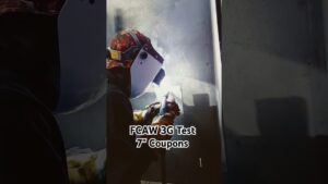 Operario con casco de soldador y guantes protegido por una visera realizando una soldadura FCAW en una plancha metálica dentro de un taller, con arco luminoso y humo visible, Ventajas y desventajas de la soldadura FCAW que debes conocer