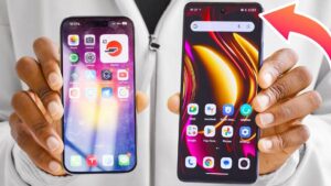 Persona sostiene con ambas manos dos teléfonos inteligentes lado a lado: a la izquierda un dispositivo con interfaz iOS y notch alargado y a la derecha un móvil Android con pantalla más amplia, fondo de pantalla colorido y cámara frontal en perforación señalada por una flecha roja, composición ideal para una comparativa visual de diseño y tamaño, perfecta para un artículo titulado Tcl 40 se ventajas y desventajas: ¿vale la pena comprarlo?